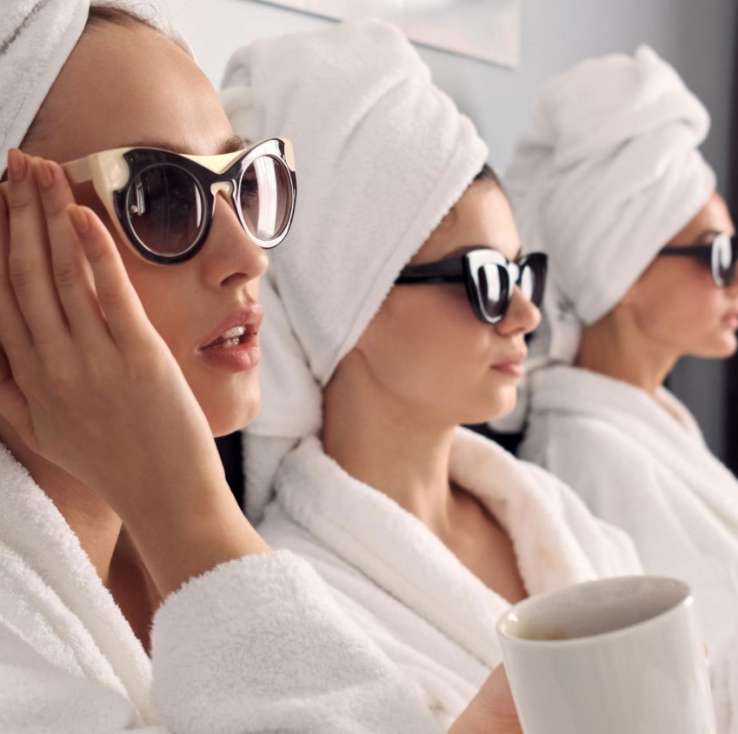 Close up beautiful girls white bathrobes with towels head sunglasses drinking coffee in a spa in Miami